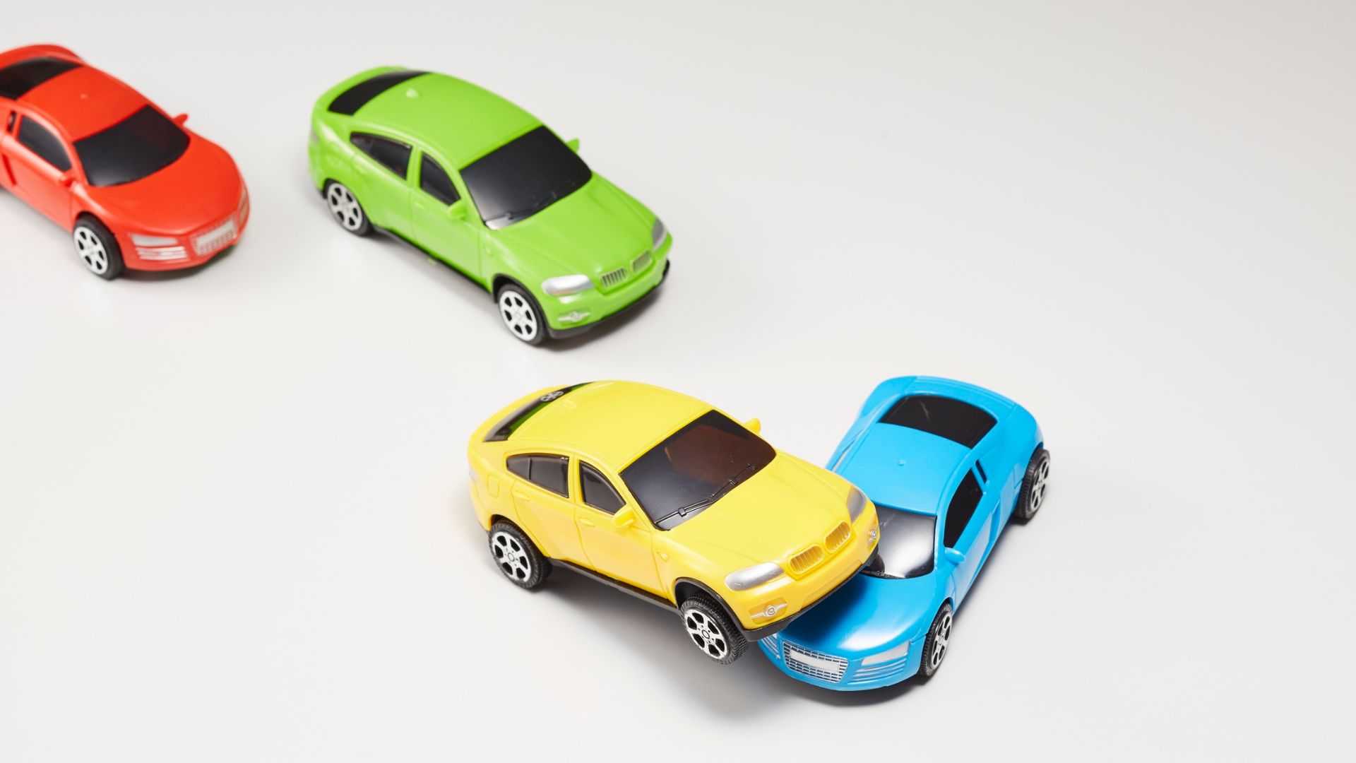 ALT描述: 四輛不同顏色的玩具車停在白色的背景上，分別是紅色、綠色、黃色和藍色，黃色和藍色玩具車發生碰撞。