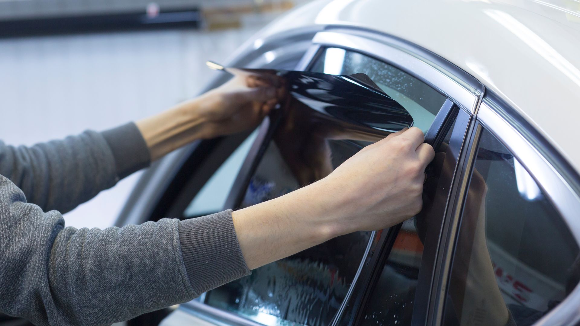 ALT描述:一個人兩隻手貼著汽車車窗，正在撕除或調整隔熱紙。