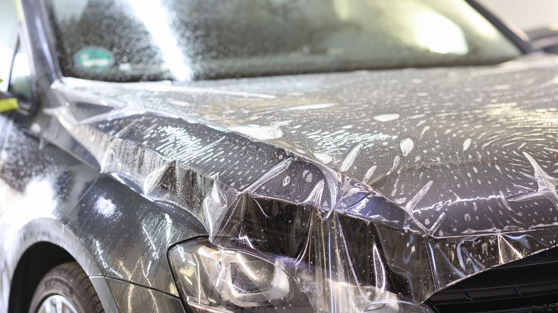 ALT描述:一張黑色的汽車引擎蓋上，覆蓋著一層透明的保護膜。膜的表面有許多小水珠和肥皂泡，表示保護膜正在施工中。