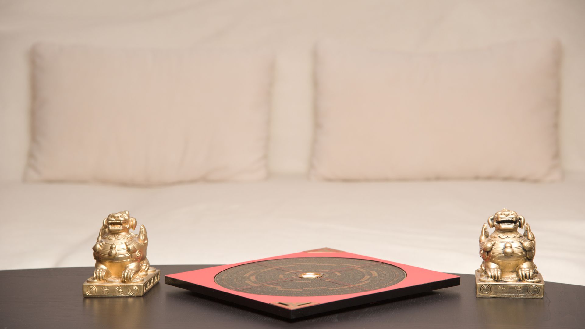 ALT描述: 室內桌上擺放著風水羅盤，兩側各有一尊金色貔貅神獸擺飾，背景為簡約的白色沙發。