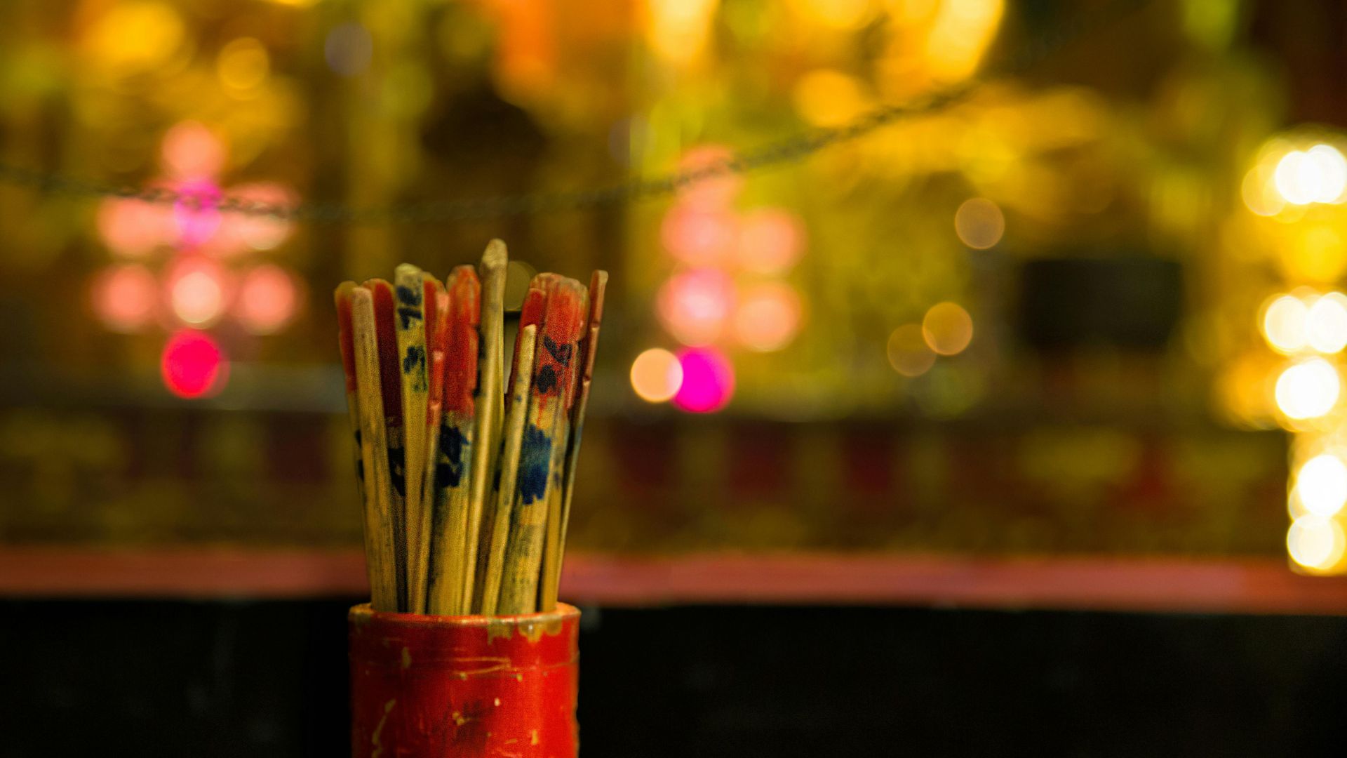 ALT描述: 特寫紅色的求籤筒，筒內裝滿了帶有標記的竹籤，背景是模糊的寺廟燈火。