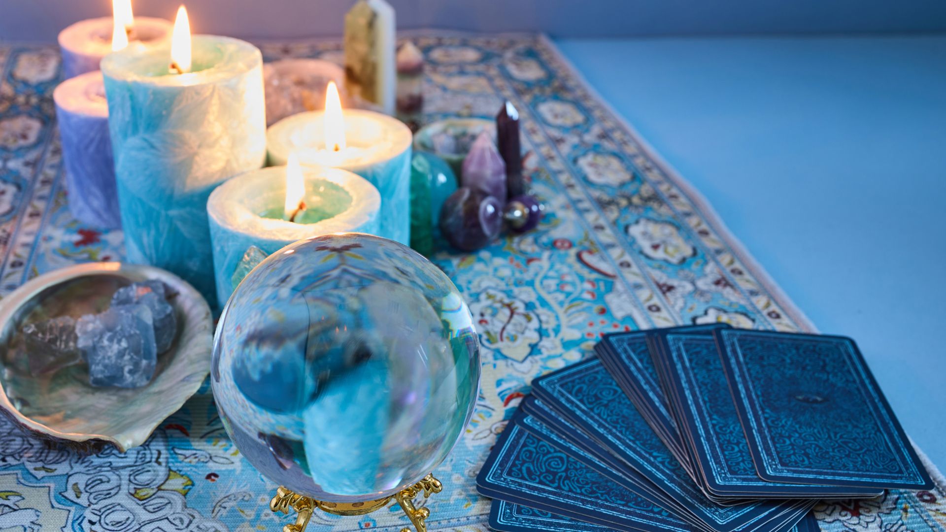 ALT描述: 占卜桌面上佈置著透明水晶球、藍色蠟燭、塔羅牌以及各種水晶簇。