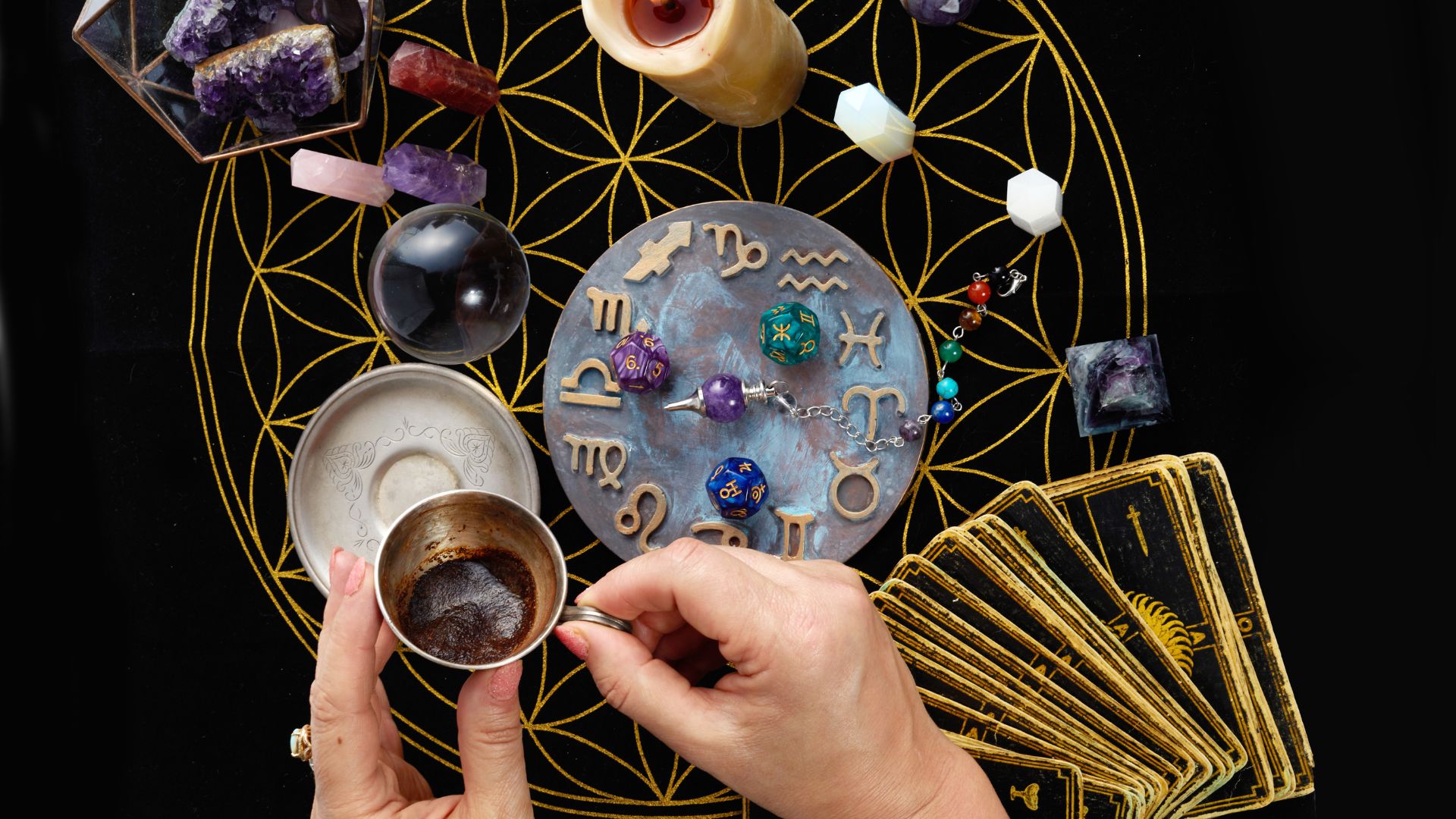 ALT描述: 從俯瞰視角拍攝占卜師的手，手中拿著咖啡杯進行占卜，案几上有星座盤、塔羅牌、靈擺與骰子。