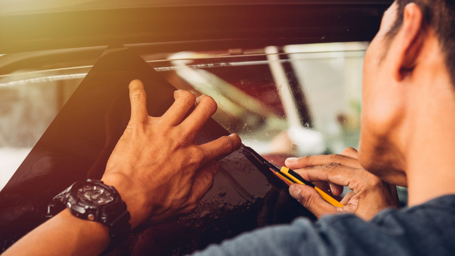 ALT描述:一個人兩隻手貼著汽車車窗，正在調整車窗隔熱紙。左手戴著手錶。