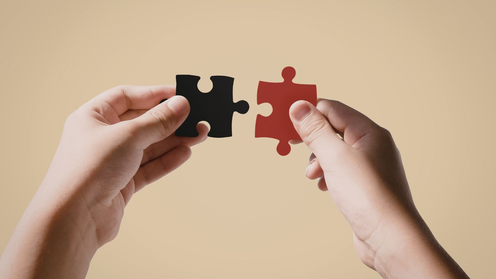 ALT描述: 兩隻手分別拿著一塊黑色拼圖與一塊紅色拼圖，在米色背景前嘗試將兩者對接，展現出連接與契合的概念。