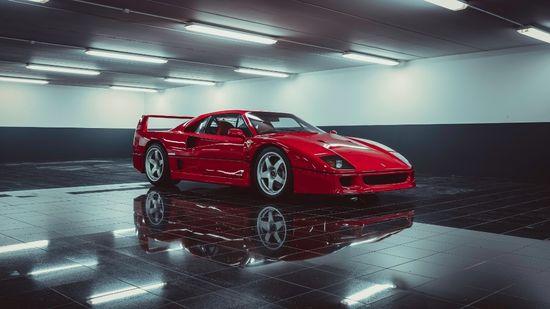 ALT描述: 一輛經典的紅色法拉利 F40 跑車停在光線充足、具有現代設計感的地下停車場內，其亮麗的車身完美地倒映在乾淨、光亮的黑色地磚上。