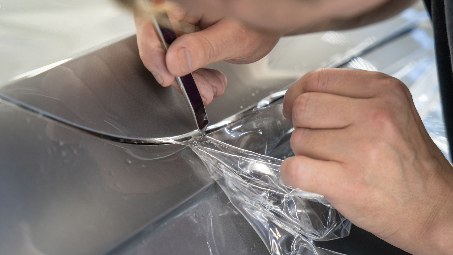 ALT描述:一個人兩隻手拿著工具，正在裁切汽車車門上的保護膜邊緣。