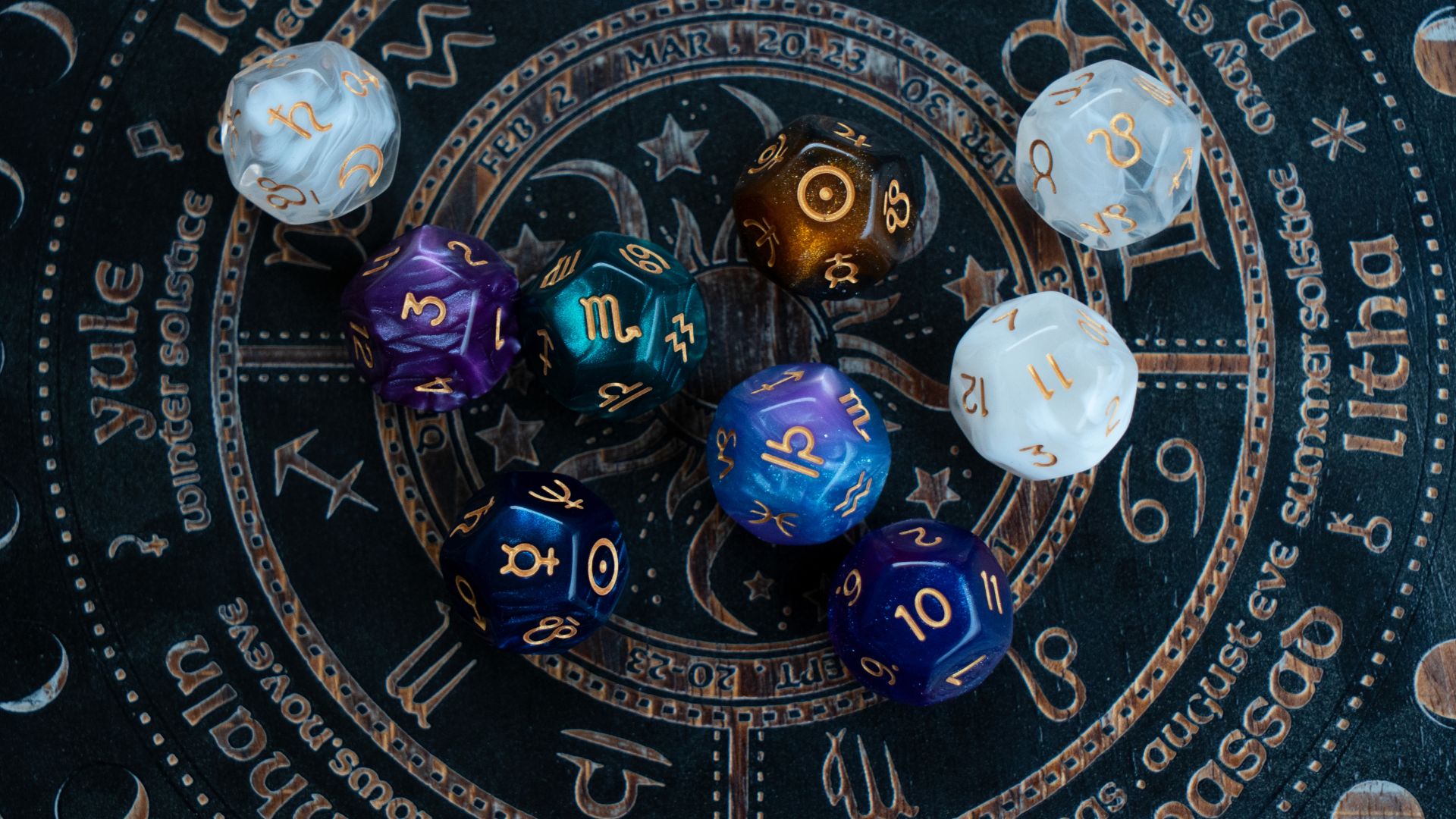 ALT描述: 黑色木質雕刻星盤上擺放著多顆彩色占卜骰子，盤面上刻有月份、星座符號以及節氣名稱如 Yule 與 Litha，充滿神祕學細節。