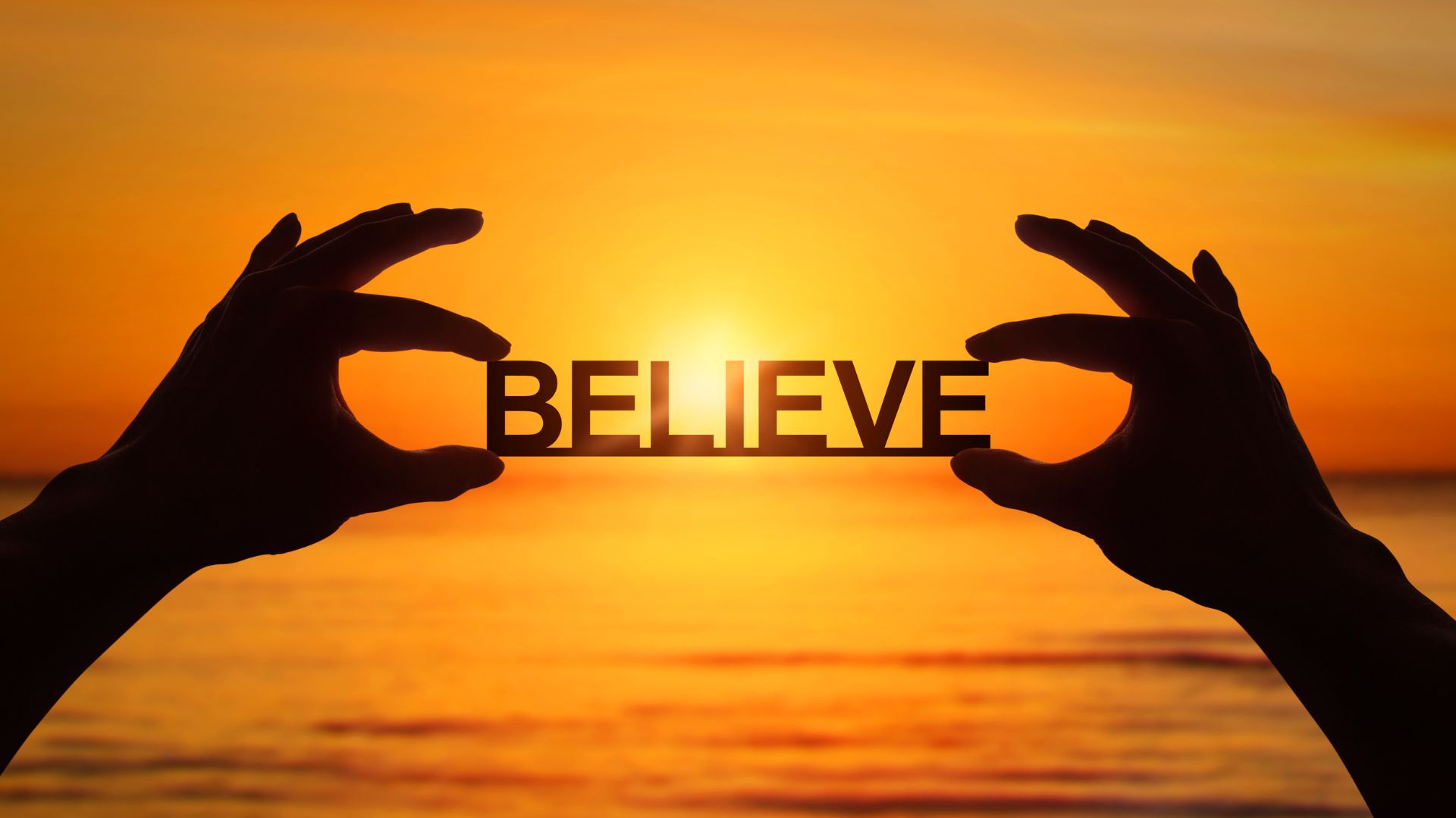 ALT描述: 雙手在夕陽餘暉的海邊背景下，高舉著「BELIEVE」字樣的剪紙標誌，光芒從字體間透出。
