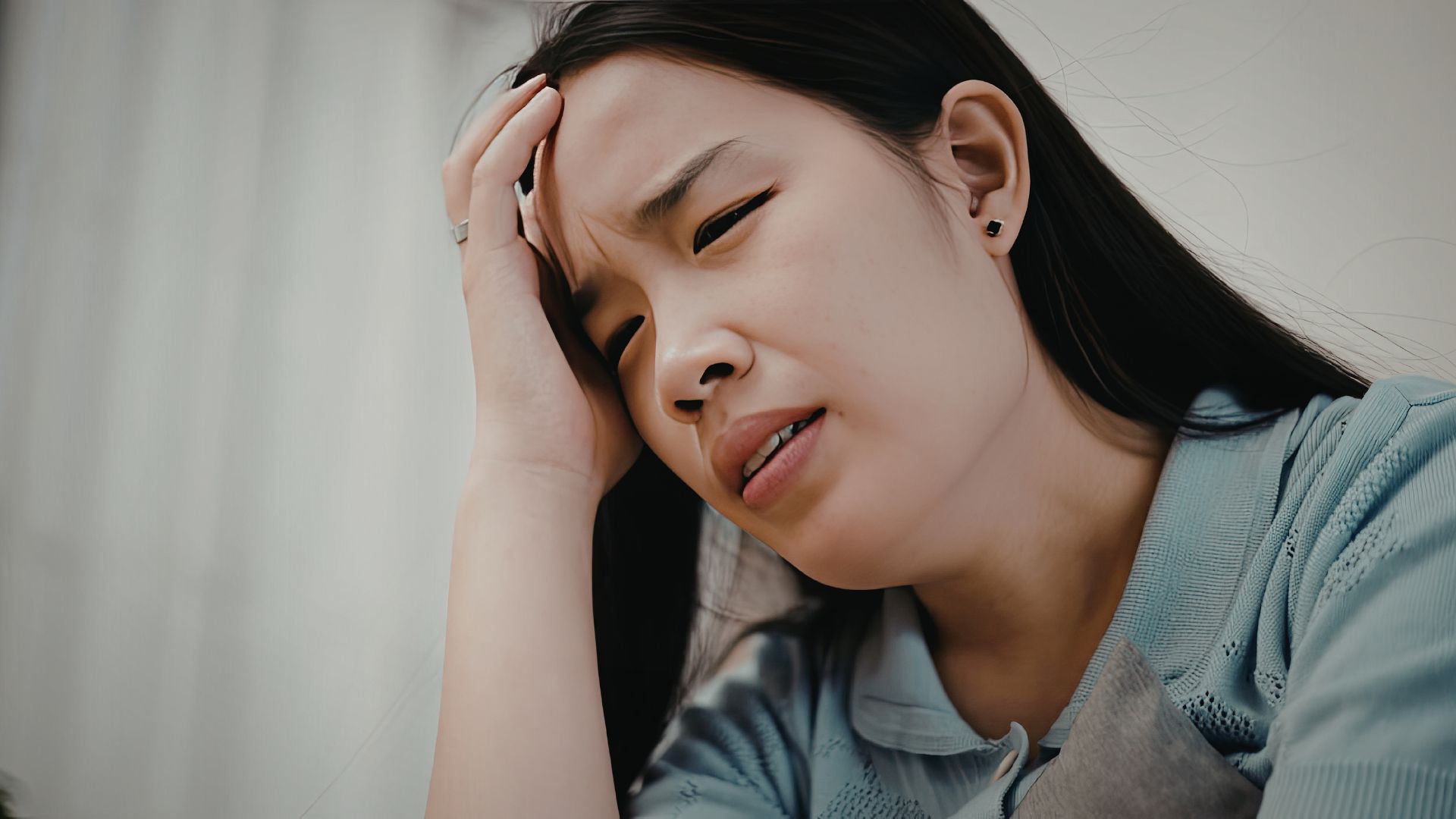 ALT描述: 一名女性眉頭深鎖、表情痛苦，右手按著前額，表現出嚴重的頭痛、偏頭痛或極度壓力的樣子。
