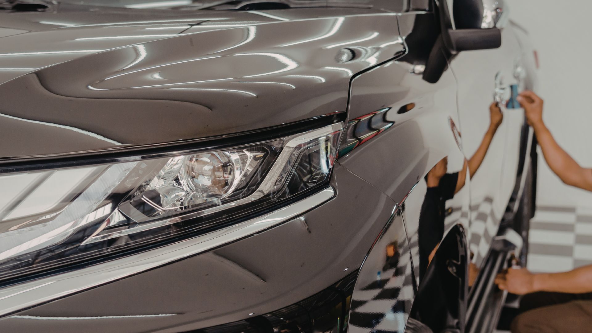 ALT描述: 汽車鍍膜後的效果展示，特寫這輛黑色休旅車犀利的大燈，倒映著車廠的條燈，背景是鍍膜施工作業。